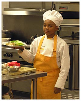 Khalil in a chef's hat and apron holding a plate of food.