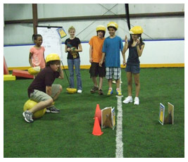 The FETCHers watch Brian bounce on an orange ball toward a goal.