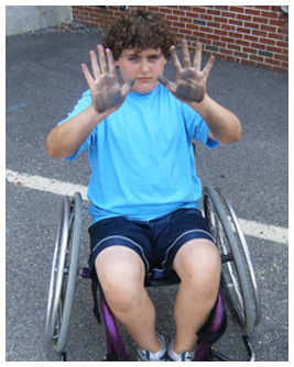 Brian sits in a wheelchair and holds up his hands.