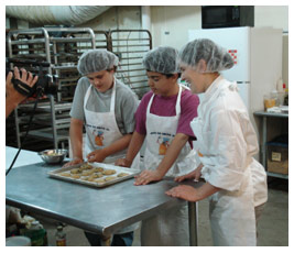 Brian, Sterling, and a chef stand at a worktable with a tray of cookies.
