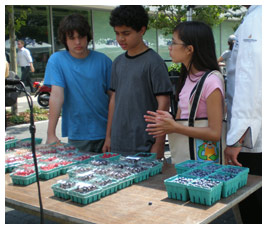 Isaac, Sterling, and Talia shop at a farmers' market. Talia's bag has a Ruff recycling symbol on it.