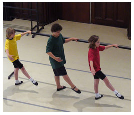 Brian and two other kids hold onto a ballet barre and point their toes.