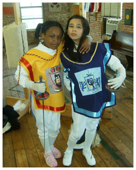 Talia and Bethany stand with their arms around each other in their fencing costumes. 