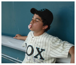 Sterling sits in a baseball dugout and blows a bubble-gum bubble.