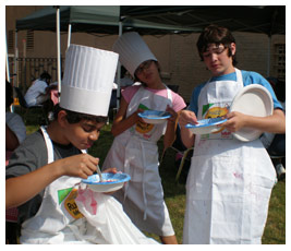 Sterling, Talia, and Isaac wear aprons and eat a snack outdoors.