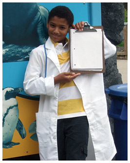 Marc wears a lab coat and holds up a clipboard.