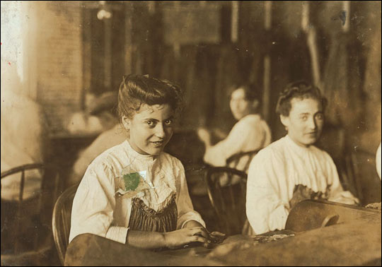 A girl sitting with other kids, rolling cigars.