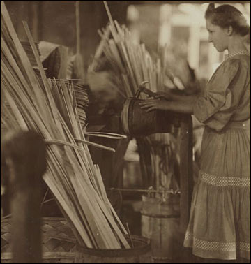 A girl standing in a factory, hammering a basket.
