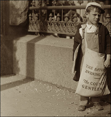 A small boy with a huge bag of newspapers.